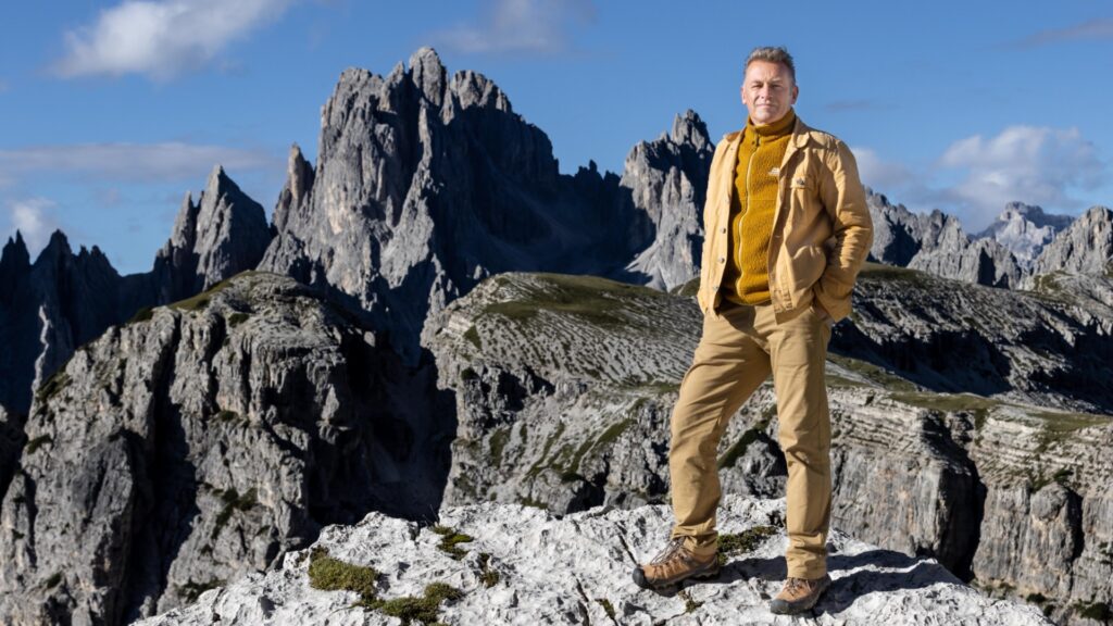 A photo of Chris Packham standing on the top of a snowy mountain
