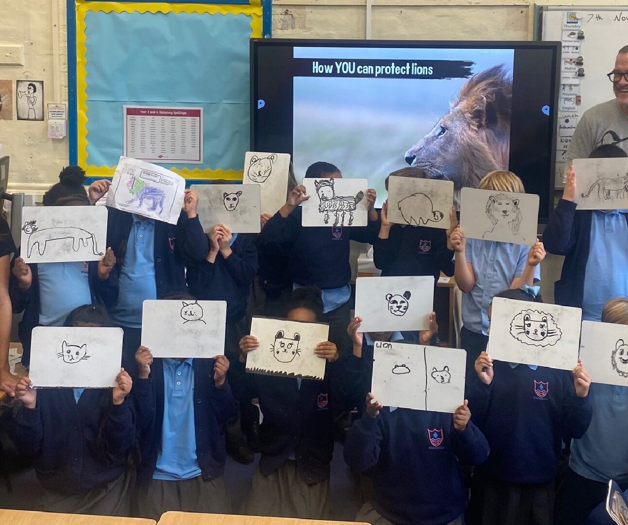 A group of school children in a classroom holding up drawings of lions.