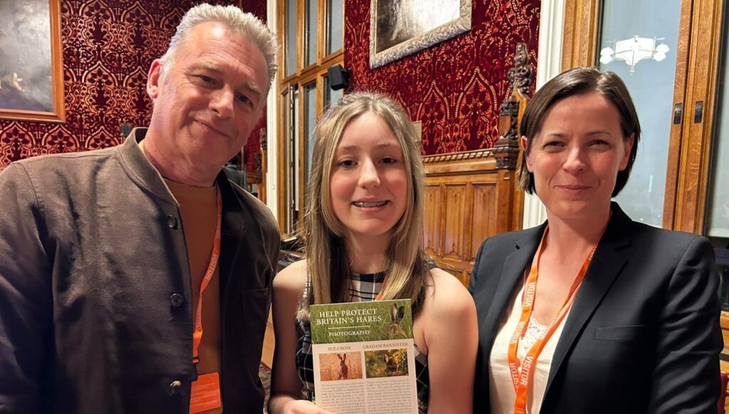 Chris Packham, Thea Caine and Chloe Dalton stood together, Thea holding a poster about hares