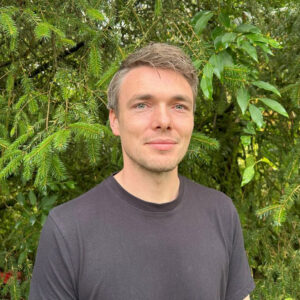 A head and shoulders photo of a man in front of a leafy background