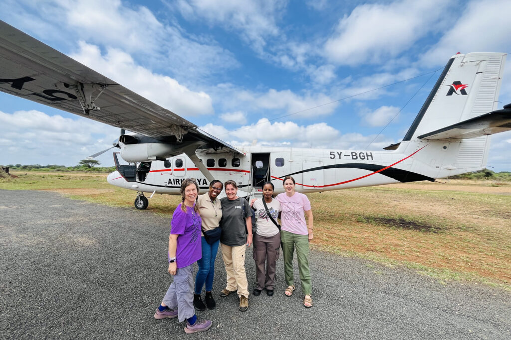 A group of five women in Born Free shirts are stood in front of an Air Kenya aeroplane 