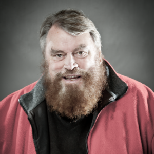 A head and shoulders photo of the actor Brian Blessed in a red jacket and black t-shirt