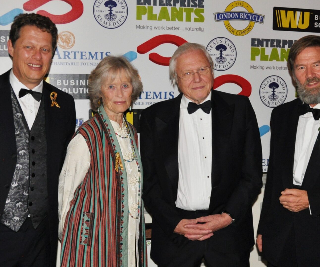 Photograph of Will Travers OBE, Dame Virginia McKenna, Sir David Attenborough, and Ian Redmond OBE, dressed in formal attire standing in front of a backdrop with multiple sponsor logos, including Artemis, Enterprise Plants, and Western Union.