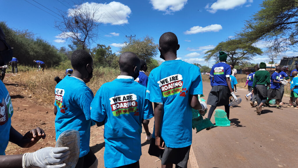 A group of young people in Blue Born Free t-shirts are walking away from the camera down a road, all holding rubbish bags ready to collect rubbish