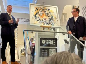 Will Travers making a speech at an art gallery event, standing in front of a painting of a tiger.