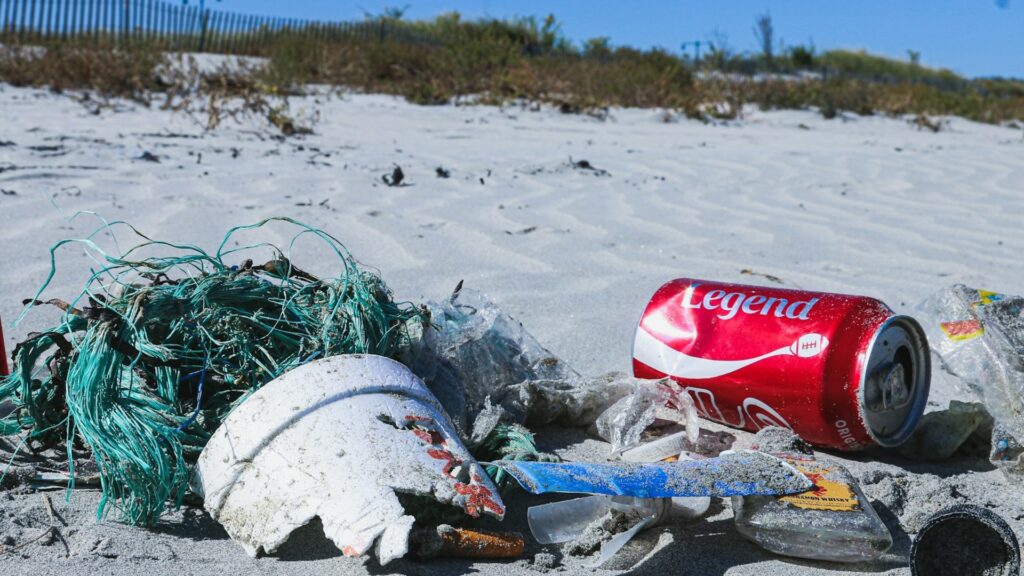 Close up of a pile of litter on the beach, including a coca cola can, fishing netting and broken pot
