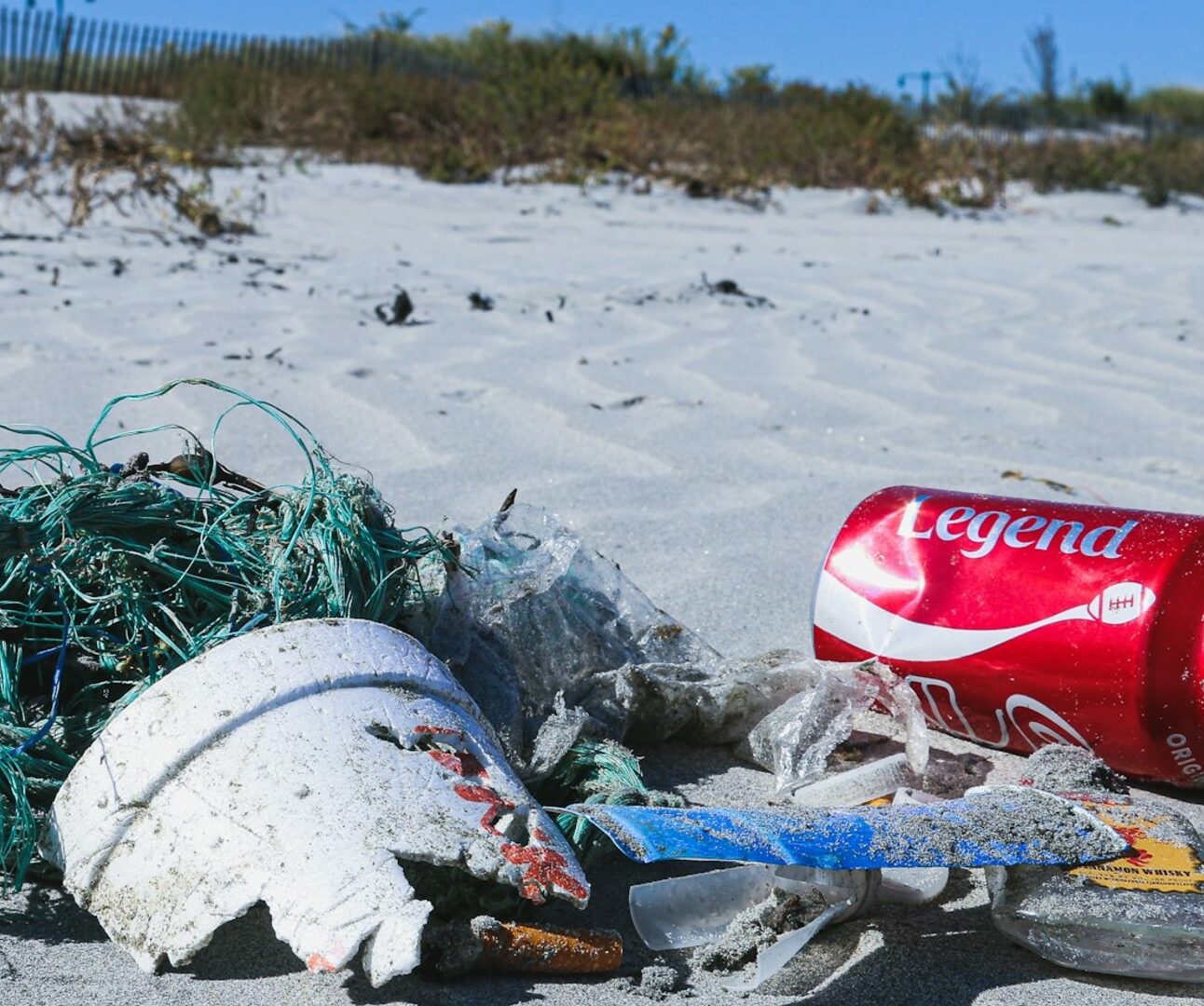 Close up of a pile of litter on the beach, including a coca cola can, fishing netting and broken pot