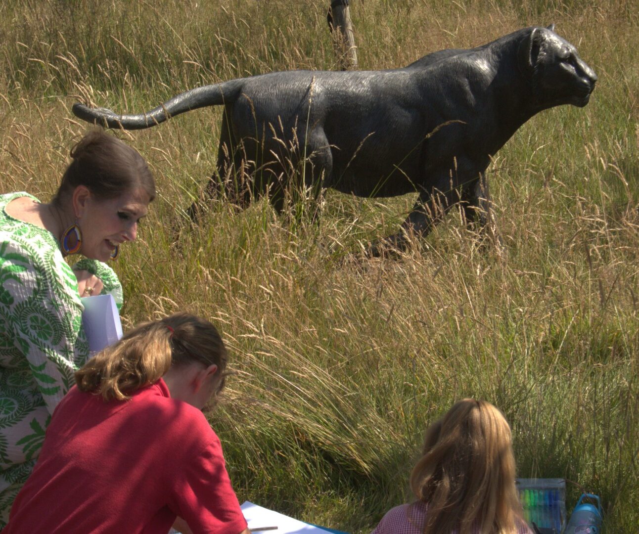 A group of young people sketching a lion statue in a field