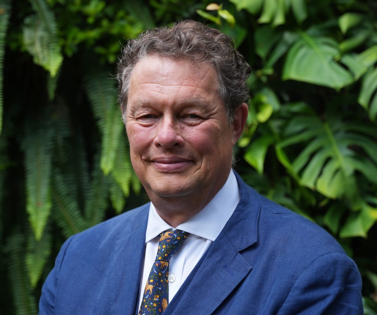 A photo of Will Travers standing in front of green foliage.